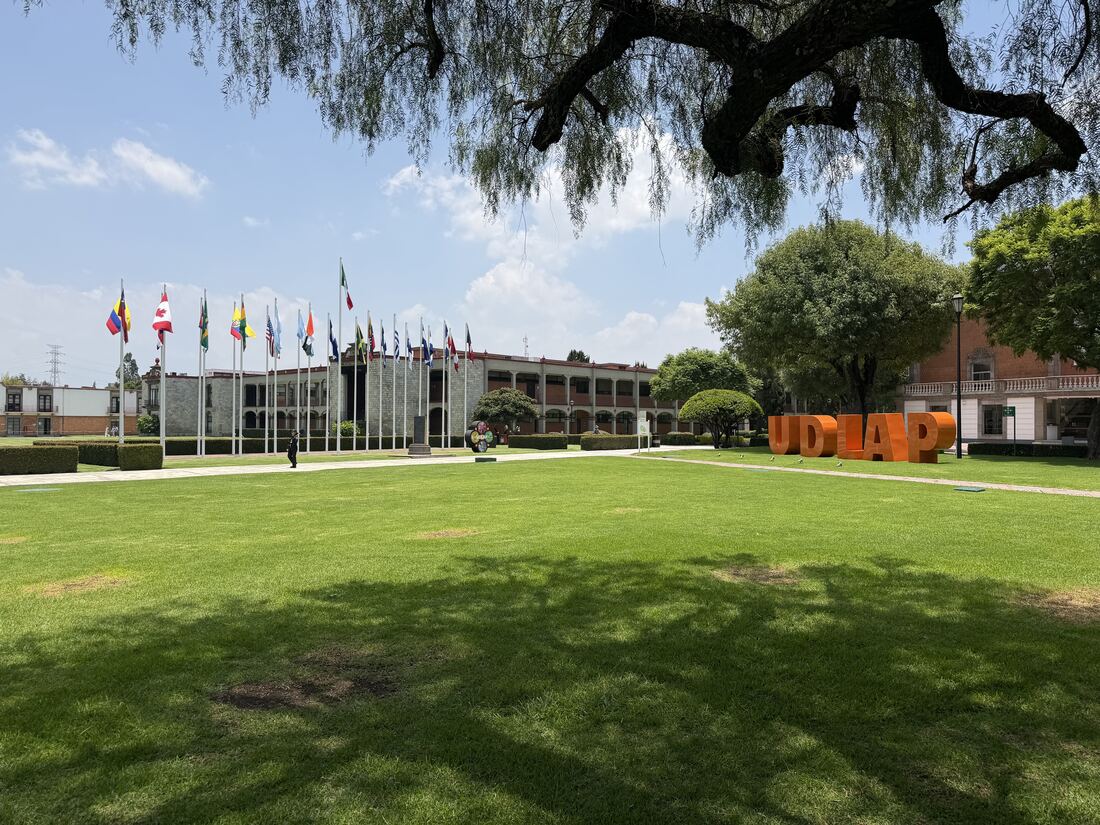 Campus der Universidad de las Américas Puebla mit Fahnenallee, Rasenfläche und dem orangefarbenen UDLAP-Schriftzug