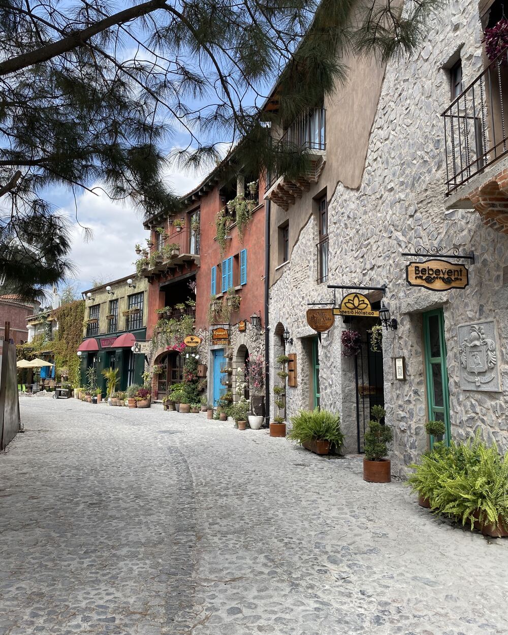 Gepflasterte Gasse mit Natursteinhäusern und Ladenschildern in Val’Quirico im Bundesstaat Tlaxcala